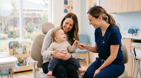 A gentle dentist welcoming a toddler on a parent's lap during a child's first dentist visit in Milwaukee