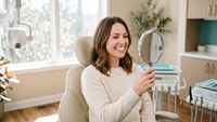 Woman admiring her brighter smile in a mirror after professional teeth whitening in Racine, WI at My Smiles USA